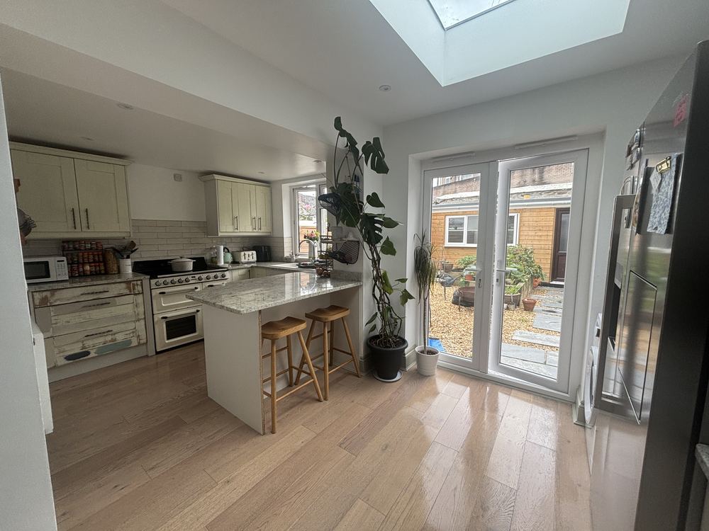 A bright, clean kitchen with a granite breakfast bar, gleaming wooden floor and garden doors