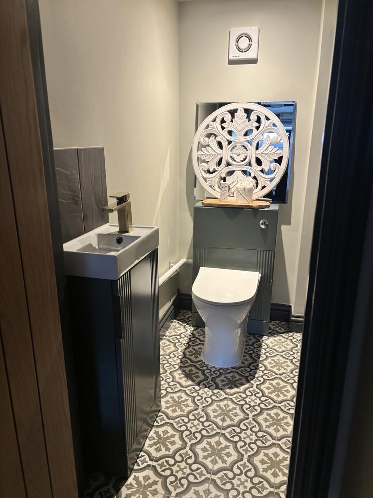A spotless cloakroom with a green vanity unit and patterned floor tiles