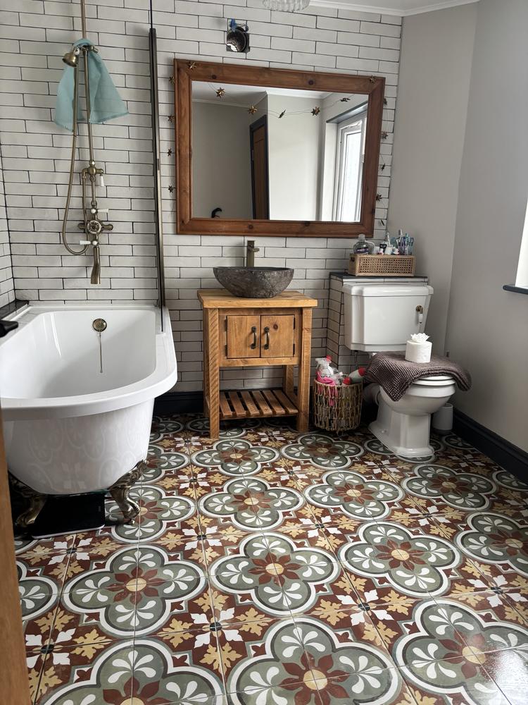 A clean bathroom with a roll-top bath, stone basin and patterned tiles