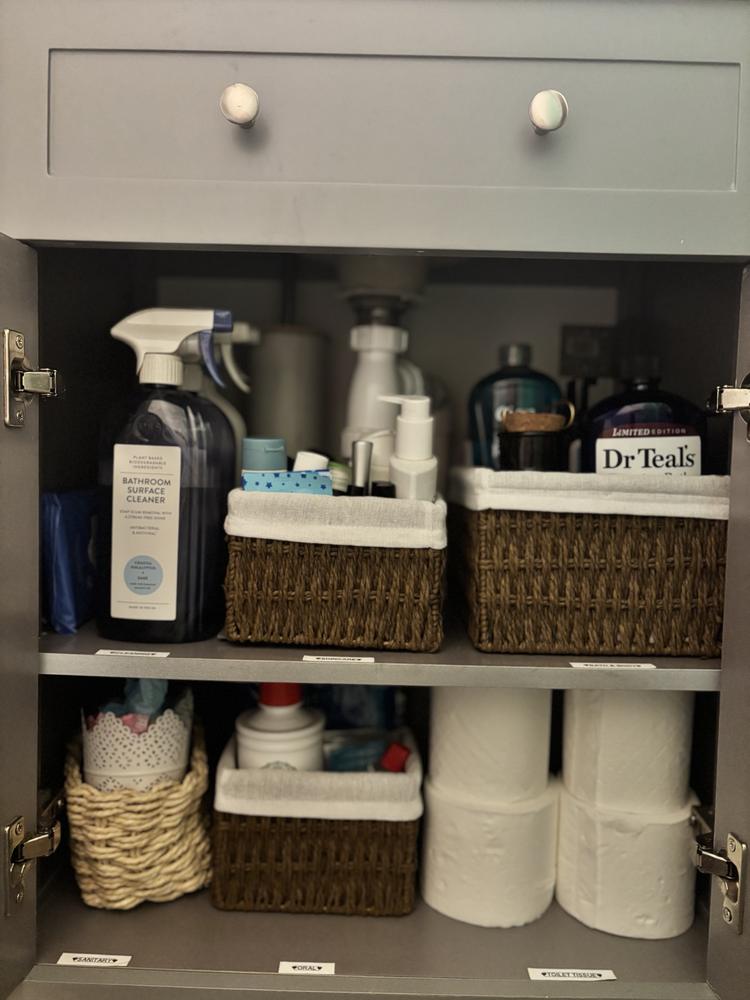 An under-sink cupboard organised into labelled wicker baskets