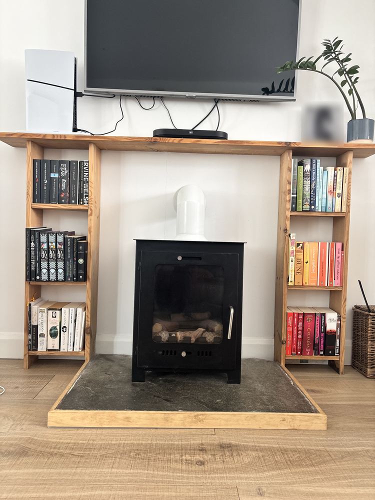 A tidy living room wood burner flanked by bookshelves with books arranged by colour